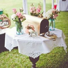 two vases with flowers are sitting on a table at an outdoor wedding reception in the grass