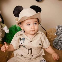 a little boy dressed up as mickey mouse sitting on the floor in front of stuffed animals