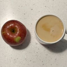 an apple sitting next to a cup of coffee on a white counter top with a brown liquid in it