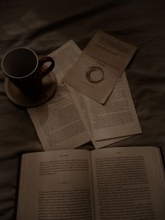 an open book sitting on top of a bed next to a cup and saucer