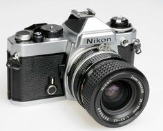 an old style camera sitting on top of a white table next to a black and silver lens