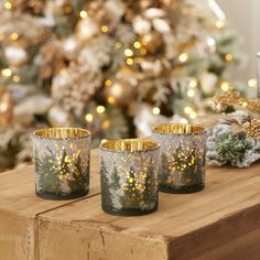 three candles sitting on top of a wooden table next to a christmas tree