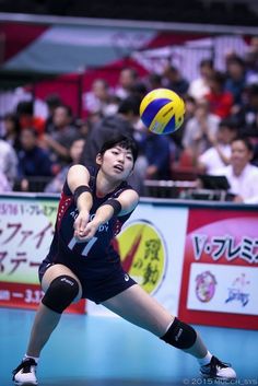 a female volleyball player in action with the ball above her head and people watching from the stands