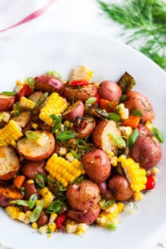 a white plate topped with potatoes, corn and green garnish on top of a table