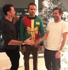 three men standing next to each other in front of a christmas tree with presents on it