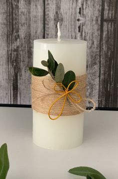 a white candle with an orange ribbon and green leaves