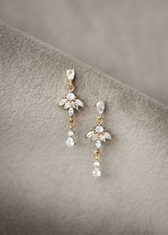 two pairs of gold and crystal earrings on top of a white cloth covered tablecloth