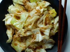 a black plate topped with cabbage covered in sauce and chopsticks next to it