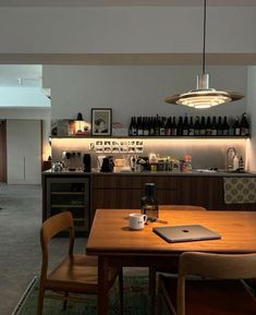 a dining room table and chairs with a laptop on top of it in front of an open kitchen area