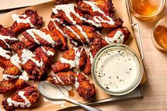 chicken wings with ranch dressing and two glasses of beer next to it on a wooden table