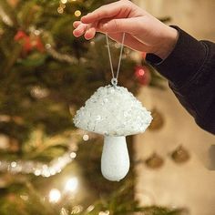 a hand holding a small white mushroom ornament in front of a christmas tree