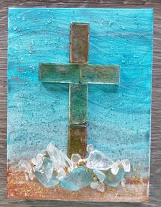 a cross made out of glass sitting on top of a piece of wood next to rocks