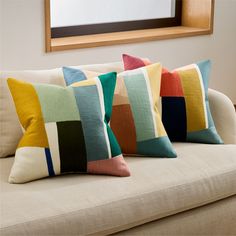 three colorful pillows sitting on the back of a couch in front of a framed mirror