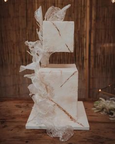 a three tiered cake with white frosting and ribbons on the top is sitting on a wooden table