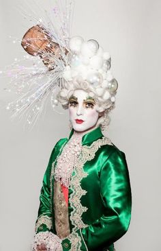 a woman wearing a green dress and white headpiece with feathers on it's head