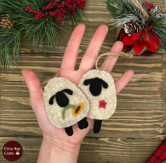 a hand holding two sheep ornaments on top of a wooden table next to christmas decorations