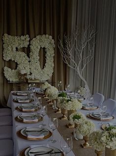 a long table is set with white flowers and gold place settings for an elegant dinner