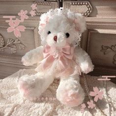 a white teddy bear with pink bows on it's head sitting on a bed