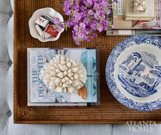 a tray with books, plates and flowers on it next to a vase filled with purple flowers