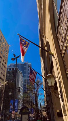 an american flag hanging from a street light in the middle of a city with tall buildings