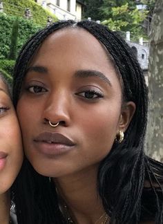 two women are posing for the camera in front of a tree and some bushes with their faces close together