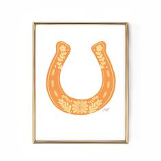 an orange horseshoe with flowers on it is mounted in a gold frame against a white wall