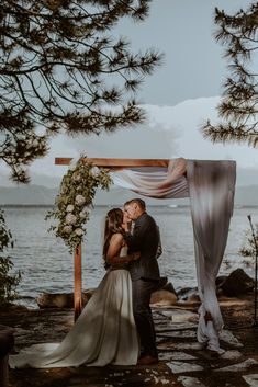 a bride and groom kissing under an arch at their wedding ceremony by the water in lake tahoe