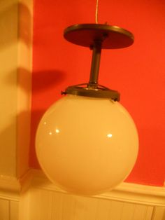 a white light hanging from a ceiling in a room with red walls and wood flooring