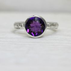 This amethyst ring is such a simple, yet dazzling piece. Though the art deco band and protective tapered bezel stone setting make for a lovely ring, the real show stopper here is the deep amethyst stone, which has vibrant internal fire and a faceted top that enhances its sparkle even further.  This stone is a generous 9mm, and it is well protected by its setting which envelops it on all sides.  I do have other stones available, too, so let me know if you're interested in a quote for something el Classic Amethyst Birthstone, Elegant Purple Amethyst Bezel Setting Ring, Elegant Purple Amethyst Ring With Bezel Setting, Purple Amethyst Art Deco Ring For Anniversary, Amethyst Birthstone Ring Round Shape, Purple Amethyst Ring With Center Stone, Amethyst Birthstone Ring With Center Stone, Art Deco Purple Amethyst Ring For Anniversary, Purple Amethyst Ring With Center Round Stone