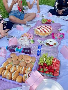 some people sitting on the grass with food and drinks in front of them at a picnic