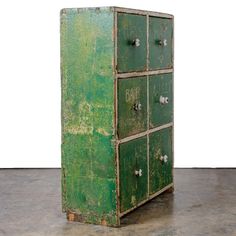 an old green metal cabinet sitting on top of a cement floor next to a white wall