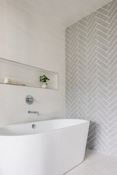 a white bath tub sitting in a bathroom next to a wall mounted shelf with a potted plant on it