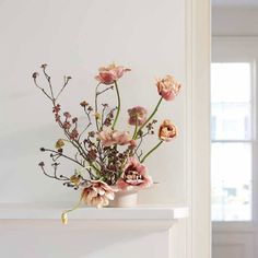 a vase filled with lots of flowers on top of a white mantle next to a window