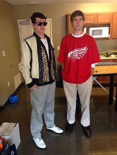 two young men standing next to each other in a room with a table and chairs