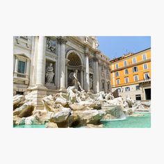 an image of a fountain in the middle of a city with yellow buildings behind it