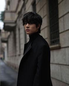 a man standing in front of a building wearing a black coat and turtle neck sweater