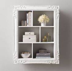 a white shelf with books and flowers in it on the wall next to a gray wall