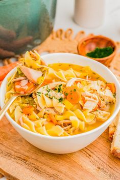 a white bowl filled with chicken noodle soup on top of a wooden cutting board