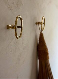 two brass hooks on a white wall with a tassel hanging from it's side