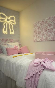 a white bed topped with pink pillows next to a wall covered in lights and decor