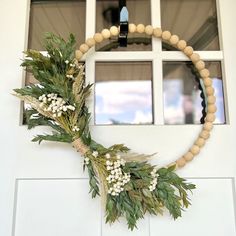 a wreath hanging on the front door of a house with white flowers and greenery