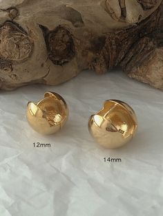 two gold earrings sitting next to each other on top of a piece of driftwood