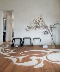 an empty room with three chairs and a vase on the floor in front of it