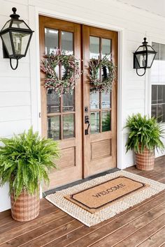 two potted plants sitting on the front porch next to a door with wreaths