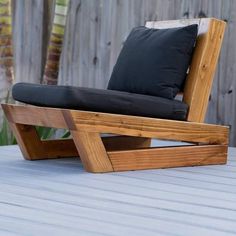 a wooden chair sitting on top of a wooden deck next to a fence with black pillows