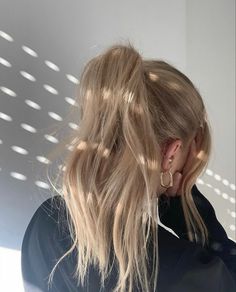 a woman with long blonde hair standing in front of a white wall