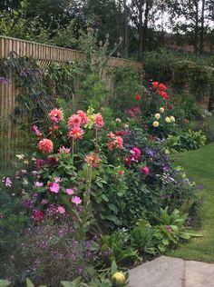 a garden filled with lots of colorful flowers next to a wooden fence and green grass