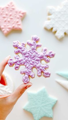 a hand holding a snowflake shaped cookie in front of other decorated sugar stars