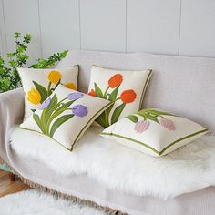 three pillows with flowers on them sitting on a couch next to a potted plant