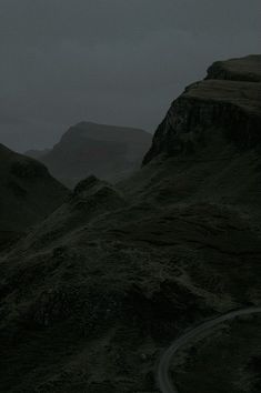 an empty road in the middle of a mountain range at night with dark clouds overhead